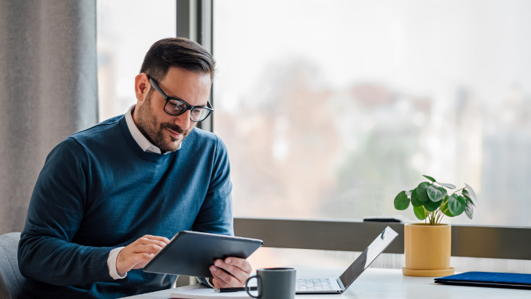 Man at table with tablet and laptop.